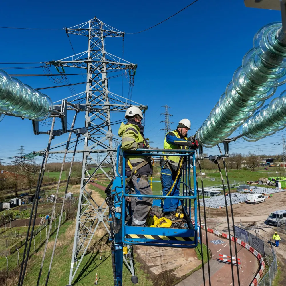 Twee mensen werken in een hoogwerker aan een hoogspanningslijn