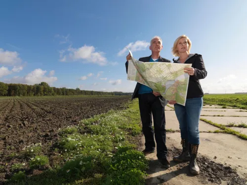 Twee personen bij een akker bekijken een landkaart